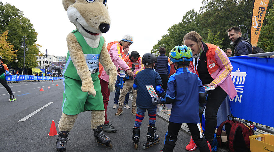 Some children with helmets and skates receive a certificate and are congratulated by the mascot Fridolin.
